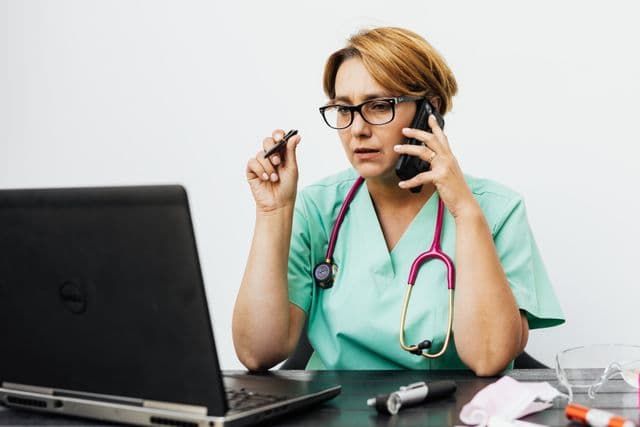 Healthcare professional speaking on the phone while working at a laptop